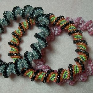 May include: Three beaded bracelets in a spiral pattern. The bracelets are black and silver, black and orange with green accents, and pink and white.