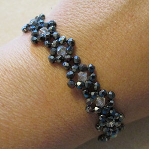 Puede incluir: Un brazalete de cuentas negras y plateadas con un diseño de flores.