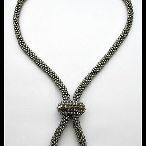 May include: A silver beaded necklace with a silver clasp and a crystal accent. The necklace is in the shape of a figure of eight.