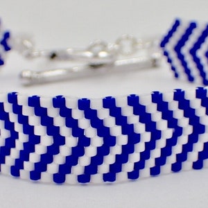 May include: A blue and white beaded bracelet with a chevron pattern. The bracelet features a silver-colored clasp. The design is a repeating pattern of blue and white beads, creating a zig-zag effect. This accessory is suitable for everyday wear.