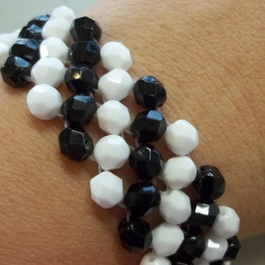 May include: A black and white beaded bracelet with a woven pattern. The bracelet is made of small, round beads that are strung together in a repeating pattern of black and white.