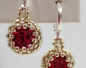 Puede incluir: Un par de pendientes de plata con cuentas de cristal rojo y cuentas de plata. Los pendientes están sobre un fondo blanco.