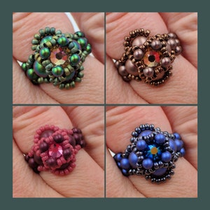 May include: Four beaded rings with different colored beads and a jewel in the center. The rings are green, brown, pink, and blue.