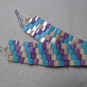 May include: A woven bracelet with a silver clasp. The bracelet is made with iridescent blue, purple, and white beads.