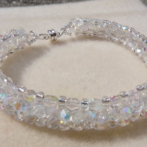 May include: A white crystal bracelet with a silver clasp. The bracelet is made of small, faceted crystals that are strung together in a spiral pattern.
