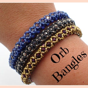 May include: Four beaded bracelets stacked on a wrist. The bracelets are made with small, colourful beads in a geometric pattern. The top bracelet is blue, the next is black, the next is gold, and the bottom is purple. The text "Orb Bangles" is written in black letters on the wrist.