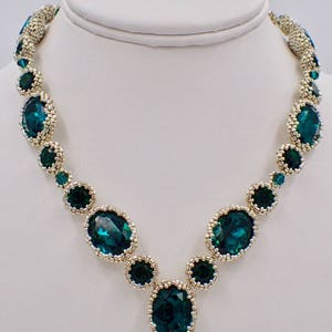 May include: A silver and emerald green beaded necklace with a v-shaped design. The necklace features large oval-shaped emerald green stones surrounded by smaller silver beads.