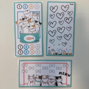 May include: Three illustrated cards with a teal border. One card features cats in a can, numbered circles, and the name "Nadine." Another has hearts and paw prints. The third card shows cats with bows and the word "MEW."
