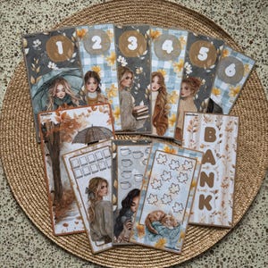 May include: A collection of rectangular paper cash envelopes featuring autumn-themed illustrations of people, umbrellas, trees, and cats. Several envelopes are numbered one through six, while others display grid patterns, leaf icons, and the word BANK.