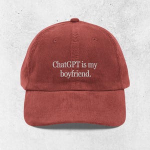 Puede incluir: Gorra de béisbol roja de pana con el texto "ChatGPT is my boyfriend" bordado en blanco. La gorra tiene una visera curva y una correa ajustable en la parte trasera.