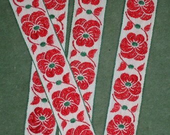 May include: Three white ribbons with red floral embroidery. The ribbons have a repeating pattern of red flowers with green leaves on a white background.