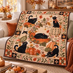 May include: A quilted throw blanket featuring a cream background with a repeating pattern of black cats, orange pumpkins, autumn leaves, and berries. The design includes a decorative border with floral motifs and geometric squares in dark colors.