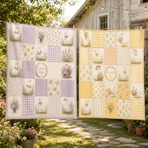 May include: Two patchwork quilts hanging on a clothesline. The left quilt features lavender and purple tones with geese, floral patterns, and the name Claire Elaine. The right quilt features yellow and gold tones with geese, floral patterns, and the name Charlotte June.