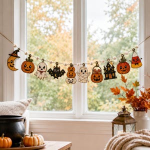 Puede incluir: Una guirnalda temática de Halloween con figuras de madera de una luna creciente, calabazas, un fantasma, un murciélago, una momia, un cubo de dulces, una casa encantada y maíz dulce, unidas por pequeñas cuentas de madera blanca en un cordel.