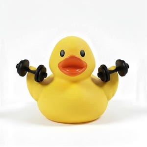 May include: A yellow rubber duck with a red-orange beak and black eyes is lifting two small black dumbbells. The duck is a novelty item, possibly a toy or decorative piece, and is set against a white background.