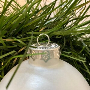 May include: A white frosted glass Christmas bauble with a silver top and a silver loop for hanging.