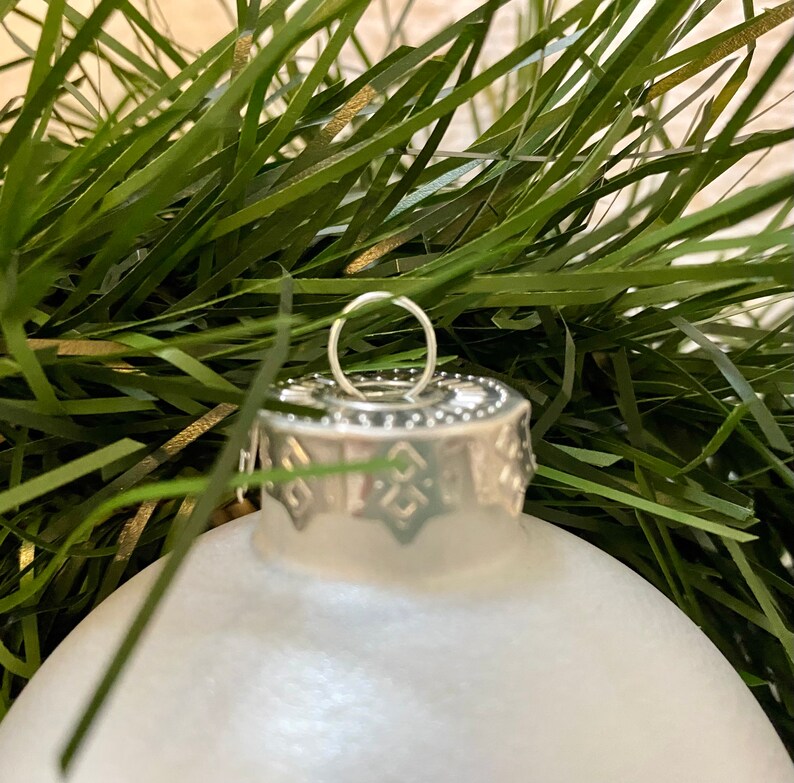 May include: A white frosted glass Christmas bauble with a silver top and a silver loop for hanging.