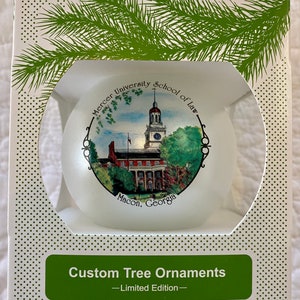 May include: White box with a green pine branch design. The box contains a white glass bauble with a printed image of Mercer University School of Law in Macon, Georgia. The bauble is a limited edition custom tree ornament.
