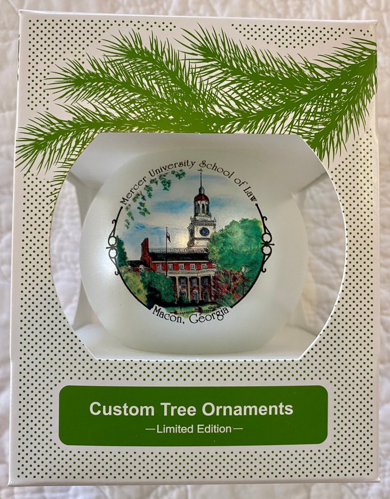 May include: White box with a green pine branch design. The box contains a white glass bauble with a printed image of Mercer University School of Law in Macon, Georgia. The bauble is a limited edition custom tree ornament.