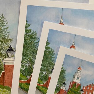 May include: Four different sizes of framed watercolour paintings of a red brick building with a white steeple and a clock tower. The building is surrounded by green trees and a brick walkway. The paintings are all signed by the artist.