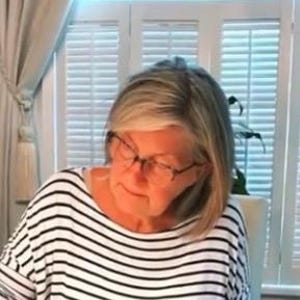 May include: A woman wearing glasses and a black and white striped shirt is looking down at something.