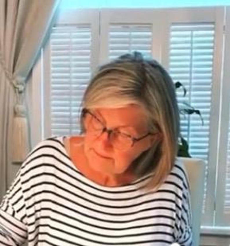 May include: A woman wearing glasses and a black and white striped shirt is looking down at something.