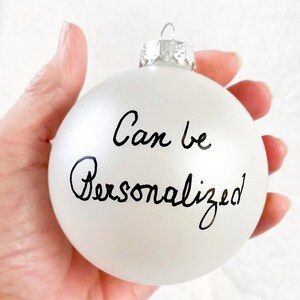 May include: White frosted glass Christmas bauble with black handwritten text that says "Can be Personalised".