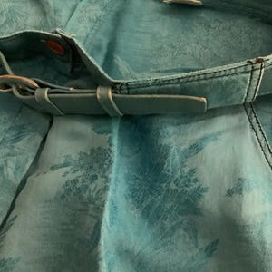 Peut inclure: Un pantalon turquoise bleu avec un motif floral et une ceinture en cuir marron. Le pantalon porte une &eacute;tiquette "Gianni Versace".