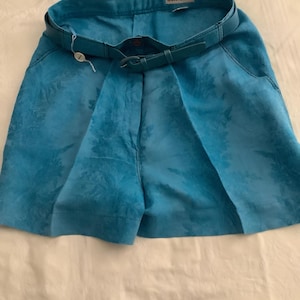 Peut inclure: Short en lin bleu avec un motif floral et une ceinture en cuir marron. Le short porte une &eacute;tiquette "Gianni Versace".