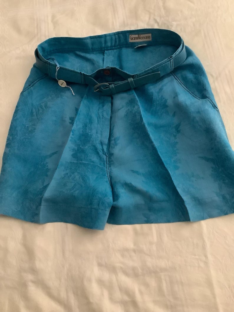 Peut inclure: Short en lin bleu avec un motif floral et une ceinture en cuir marron. Le short porte une &eacute;tiquette "Gianni Versace".