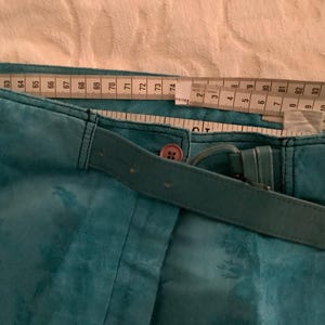 Peut inclure: Pantalon bleu sarcelle avec une ceinture assortie et un bouton marron. Le pantalon a un motif floral et est mesur&eacute; avec un m&egrave;tre ruban.