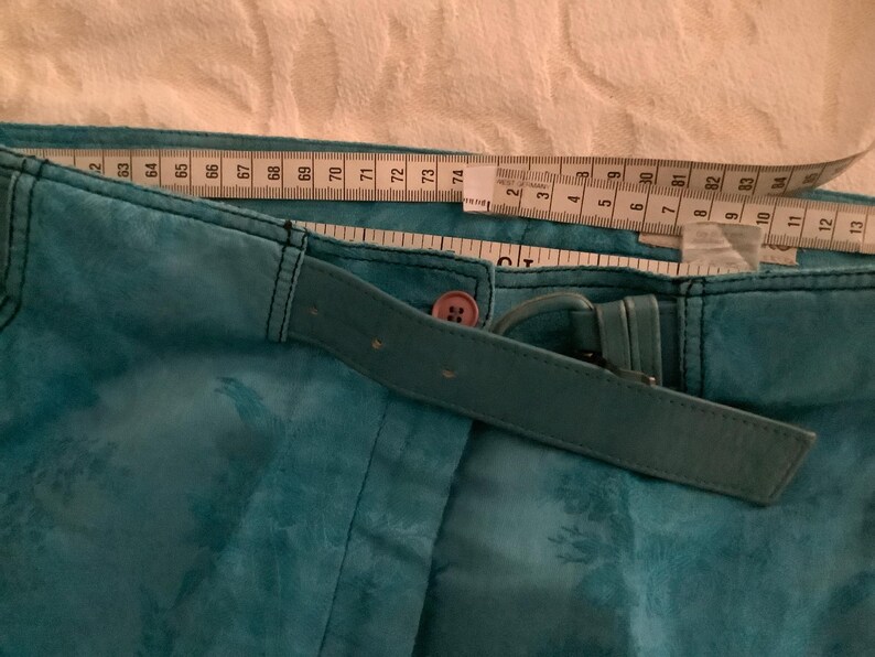 Peut inclure: Pantalon bleu sarcelle avec une ceinture assortie et un bouton marron. Le pantalon a un motif floral et est mesur&eacute; avec un m&egrave;tre ruban.