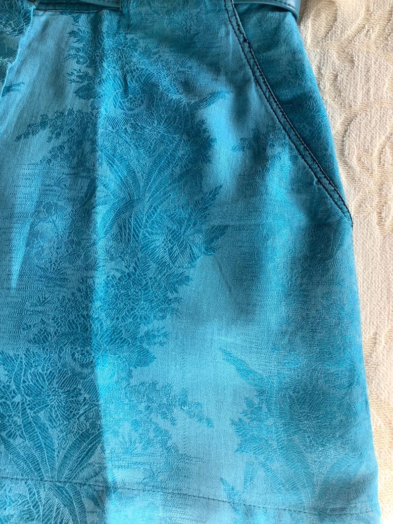Peut inclure: Une jupe bleu turquoise &agrave; motif floral. La jupe a une ceinture et deux poches.