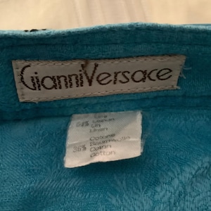 Peut inclure: Un tissu bleu turquoise avec une &eacute;tiquette blanche qui dit "Gianni Versace" et une plus petite &eacute;tiquette blanche avec le texte "Care 64% Linen 36% Cotton Ramie Cotton Cotton".