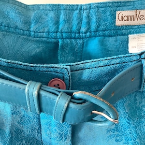 Peut inclure: Un short en jean bleu avec une ceinture en cuir bleu et une &eacute;tiquette Gianni Versace. Le short a un motif floral.