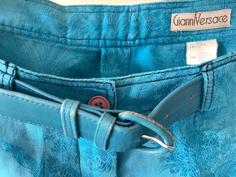 Peut inclure: Un short en jean bleu avec une ceinture en cuir bleu et une &eacute;tiquette Gianni Versace. Le short a un motif floral.