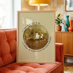 May include: A framed rectangular wall art print featuring a central gold disco ball illustration. The text surrounding the disco ball reads: IT'S GONNA BE YOU & ME, IT'S GONNA BE EVERYTHING YOU EVER DREAMED. The print is set in a light wood frame.