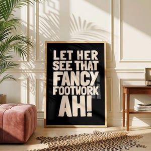 Può includere: Una stampa da parete rettangolare in una cornice di legno chiaro con sfondo nero e testo in grassetto color crema che recita: LET HER SEE THAT FANCY FOOTWORK AH!