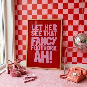 May include: A rectangular framed wall art piece with a red background and light pink text that reads LET HER SEE THAT FANCY FOOTWORK AH! The print is displayed alongside pink platform heels, two cassette tapes, and a coral rotary telephone.