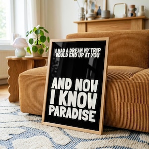 May include: A rectangular framed wall art piece featuring a black background with bold white text that reads: I HAD A DREAM MY TRIP WOULD END UP AT YOU AND NOW I KNOW PARADISE. The frame is made of light-coloured wood and has a clean, simple border.