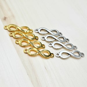 May include: Gold and silver-colored infinity symbol charms. The charms are arranged in rows, with the gold charms on the left and the silver charms on the right. Each charm has a loop on each end for attaching to other items.