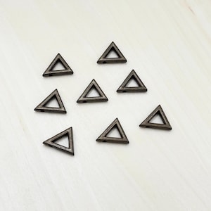 May include: Eight silver triangle-shaped charms with a hole in the center. The charms are arranged in a semi-circle on a light wood surface.