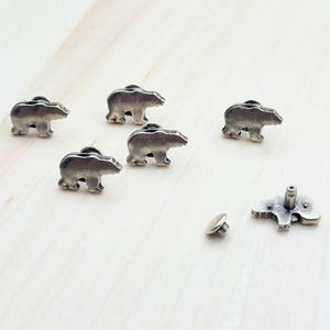 May include: Five silver metal bear-shaped rivets with a single silver metal rivet base and post. The rivets are for leather crafting.