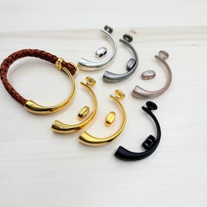 May include: Assortment of six metal bracelet clasps in various finishes, including gold, silver, black, and rose gold. Each clasp features a curved design with a small, round button.
