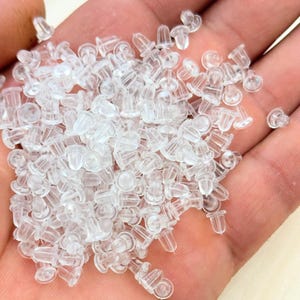 May include: A handful of clear, translucent earring backs. The earring backs are small, with a rounded base and a post-receiving hole. They are made of a soft, flexible plastic material.