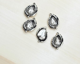 May include: Five silver teardrop-shaped pendant charms with a textured surface and a loop at the top for attaching to jewelry.
