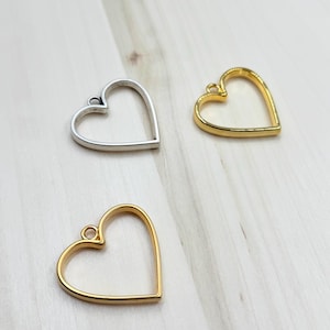 Puede incluir: Tres marcos de metal en forma de corazón, dos dorados y uno plateado, con un bucle en la parte superior para colgar.