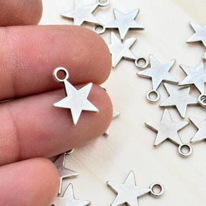 May include: Silver star charms with a jump ring for attaching to jewelry or crafts. The charms are scattered on a white surface.