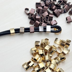 May include: A close-up of two rows of metal cord end caps. The top row has copper-colored end caps and the bottom row has gold-colored end caps. A black leather cord is threaded through the end caps.