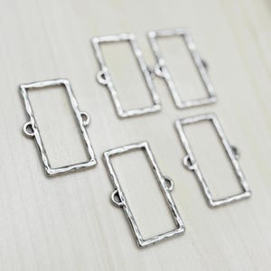 May include: Six silver-toned metal rectangular frames with a hammered texture. The frames have two small loops on the top and bottom for attaching to jewelry or other crafts.